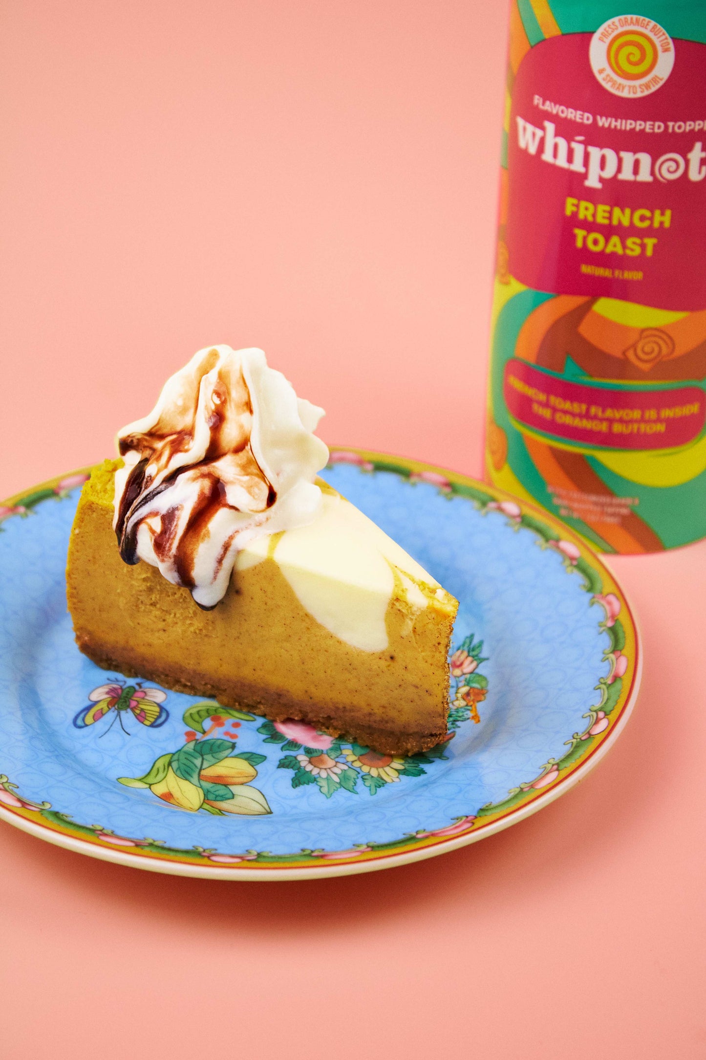 
                  
                    Slice of cake with whipped cream and chocolate sauce on a floral plate, next to a can of whipped cream topping.
                  
                
